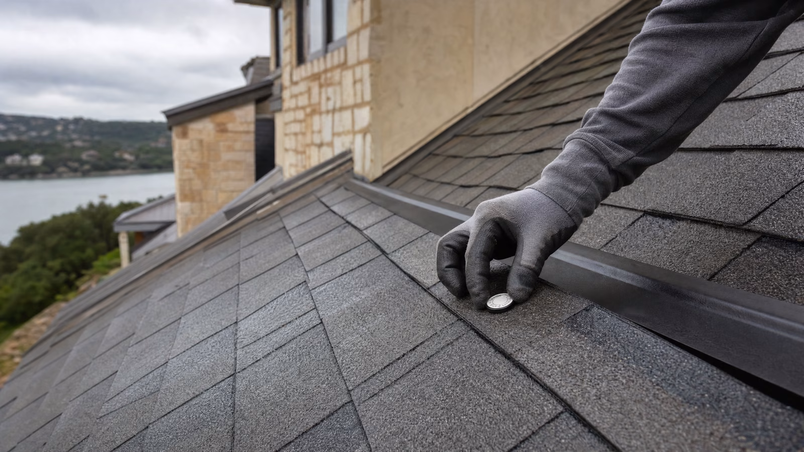 Gloved roof inspector examining an impact mark on architectural shingles above Lake Travis